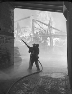 402771 Afbeelding van twee brandweerlieden tijdens het blussen van een brand bij Houthandel Jongeneel (Zeedijk 6) te Utrecht.